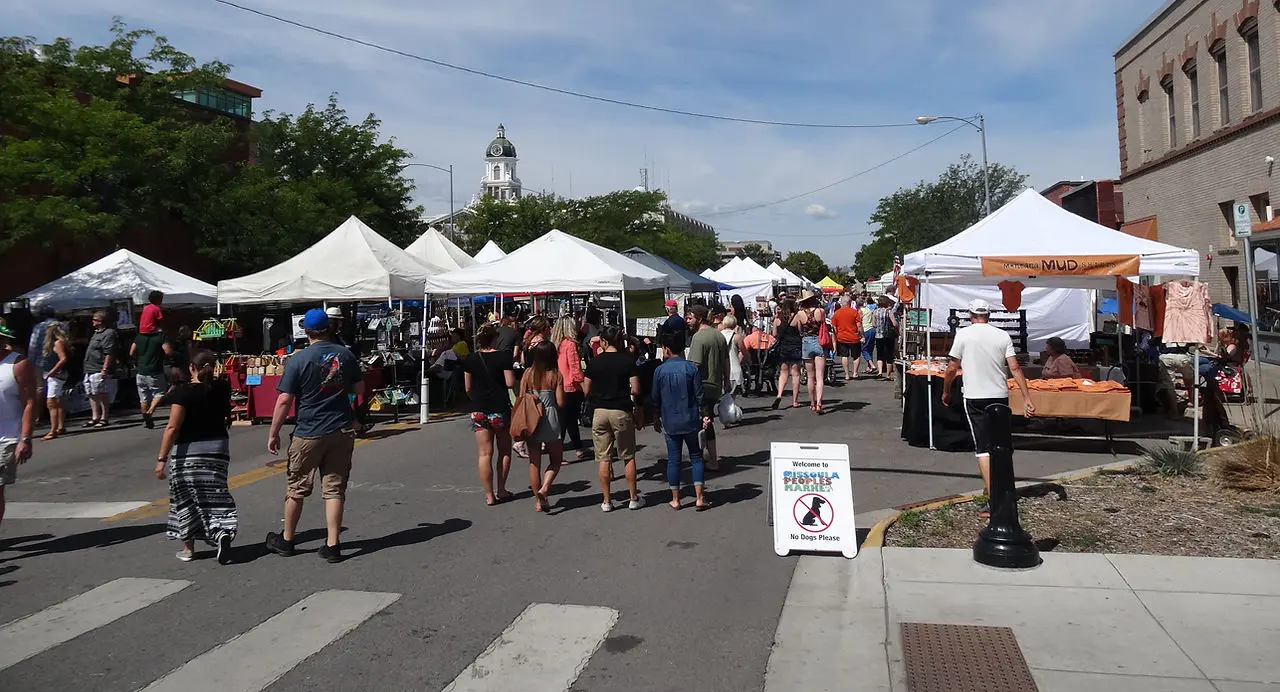 People stroll through an outdoor street market with various white vendor tents.