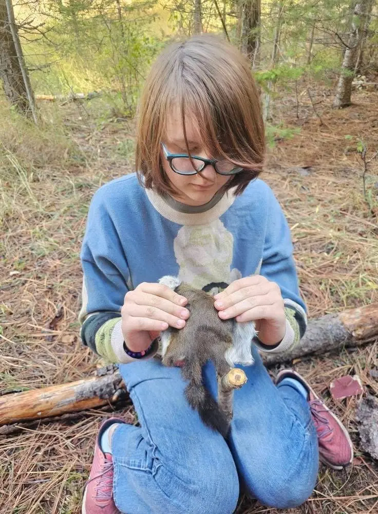 A person kneels in the woods while holding a small animal specimen.