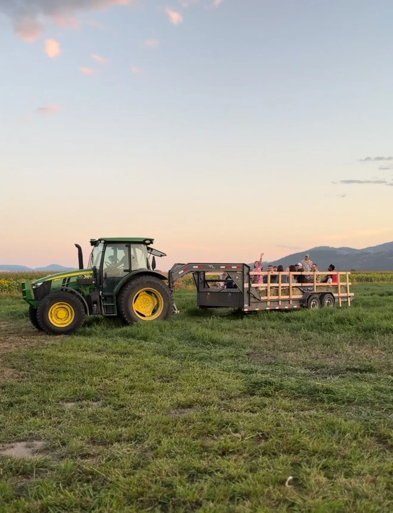 A tractor pulls a trailer full of people through a field at sunset.