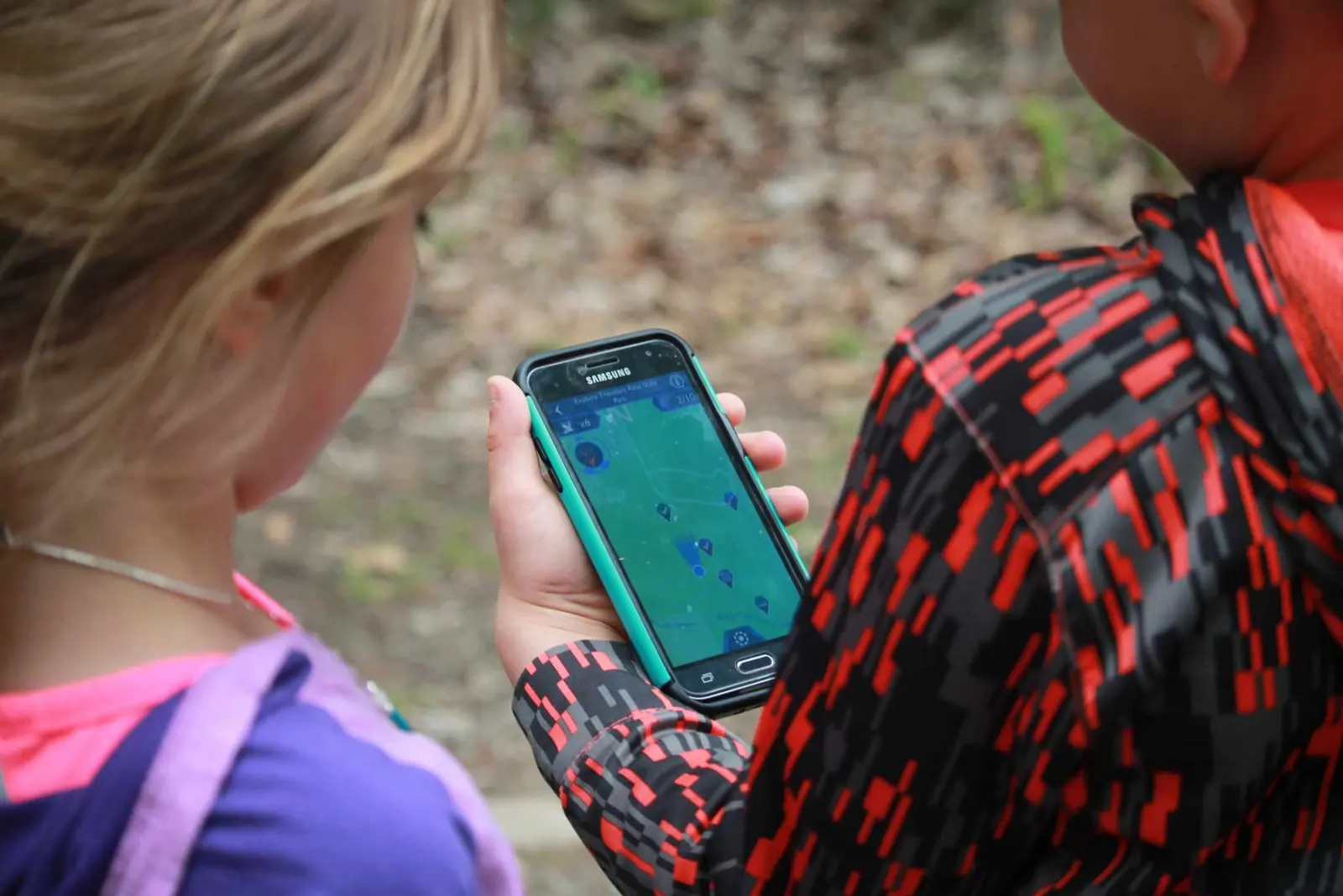 Two children look at a map displayed on a smartphone screen outdoors.