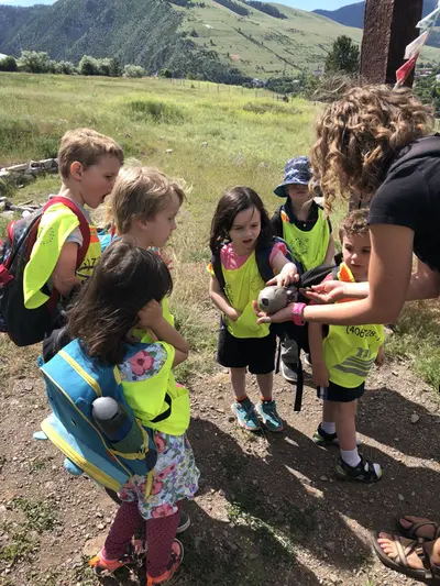 An instructor leads a group of children in yellow safety vests on an outdoor exploration.