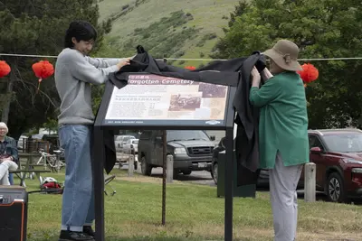Photo from ypradio.org Kim and his grandmother, who made the trip from Seoul, South Korea, lift the cover from the newly installed plaque in Missoula’s Gregory Park on June 6.