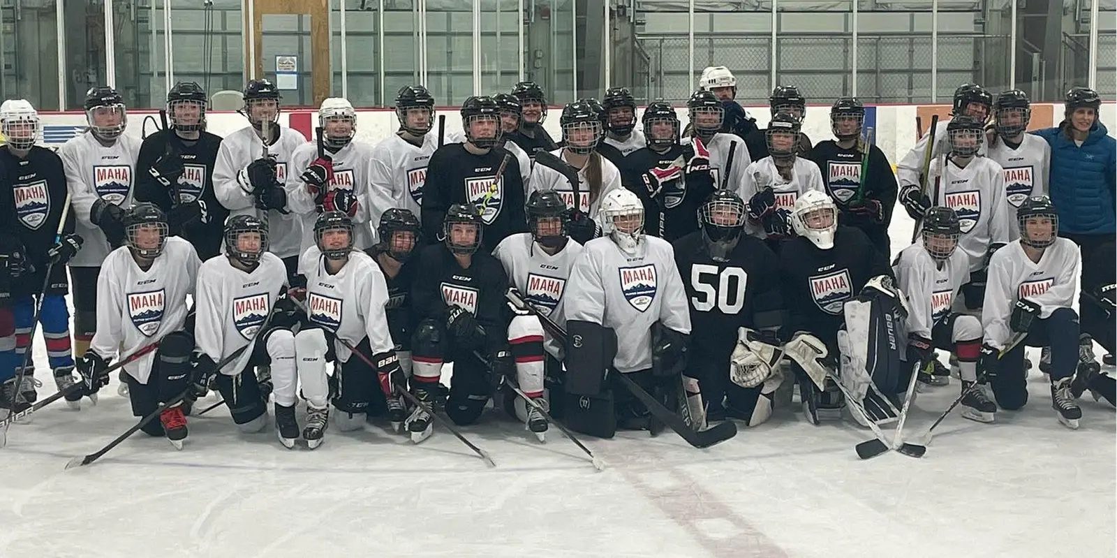 A large group of youth ice hockey players and their coach pose for a team photo on the ice rink.