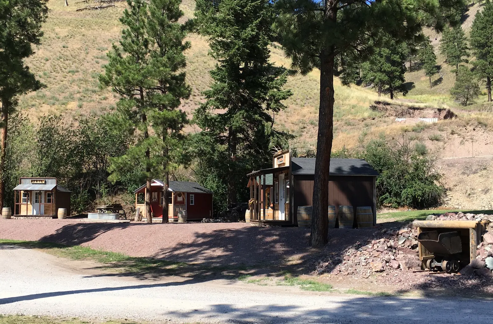 A collection of small rustic wooden buildings situated in a clearing near a hillside.
