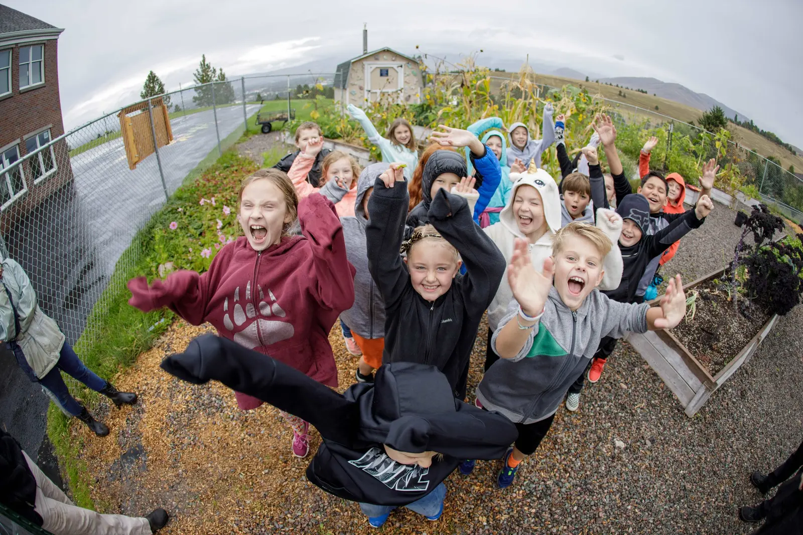 A large group of children outdoors excitedly waving their arms toward the camera.