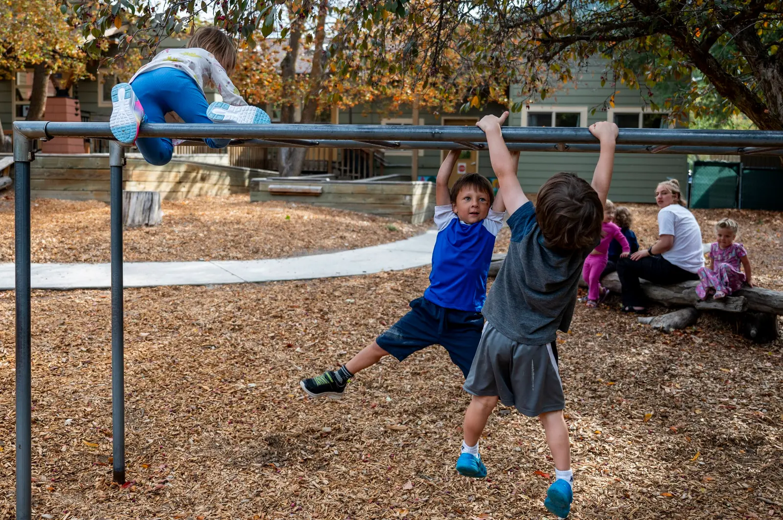Children play on a metal bar structure in an outdoor play area.