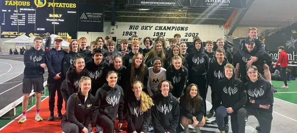 A group of young athletes in matching hoodies posing together on an indoor track.