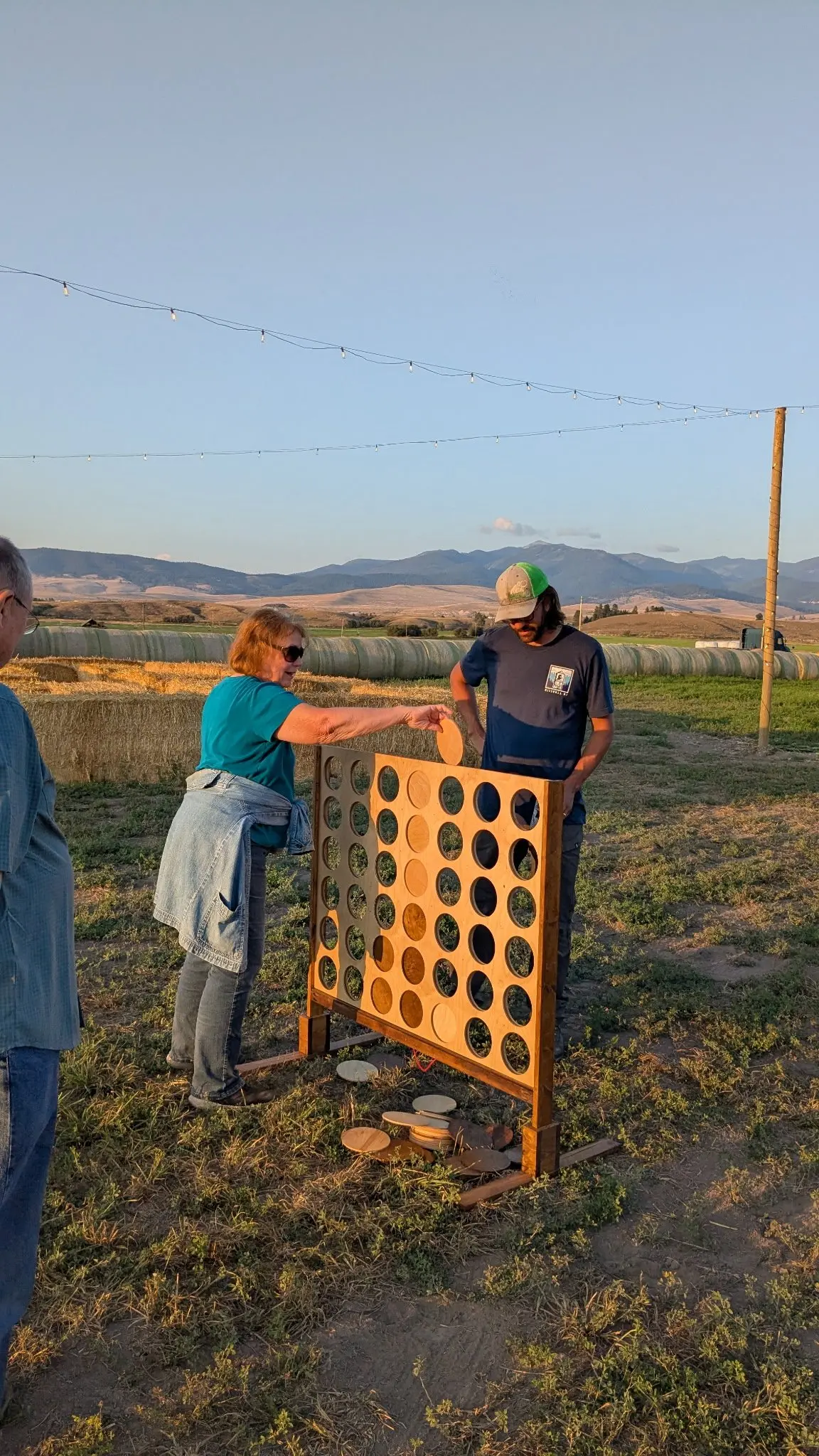 A woman and a man play a large outdoor connect-four style game in a rural field.