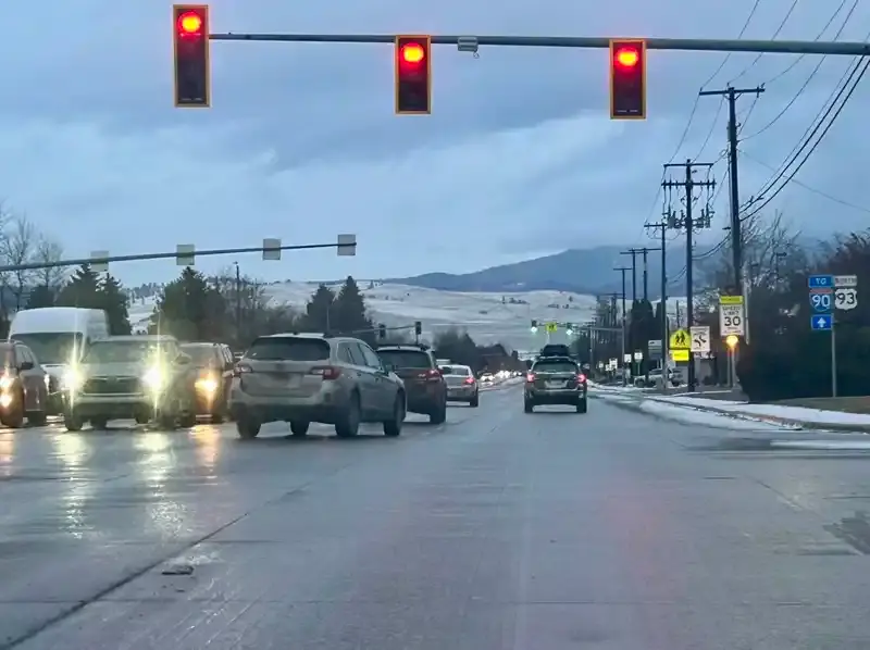Cars wait at a red light on a road with snowy hills in the background.