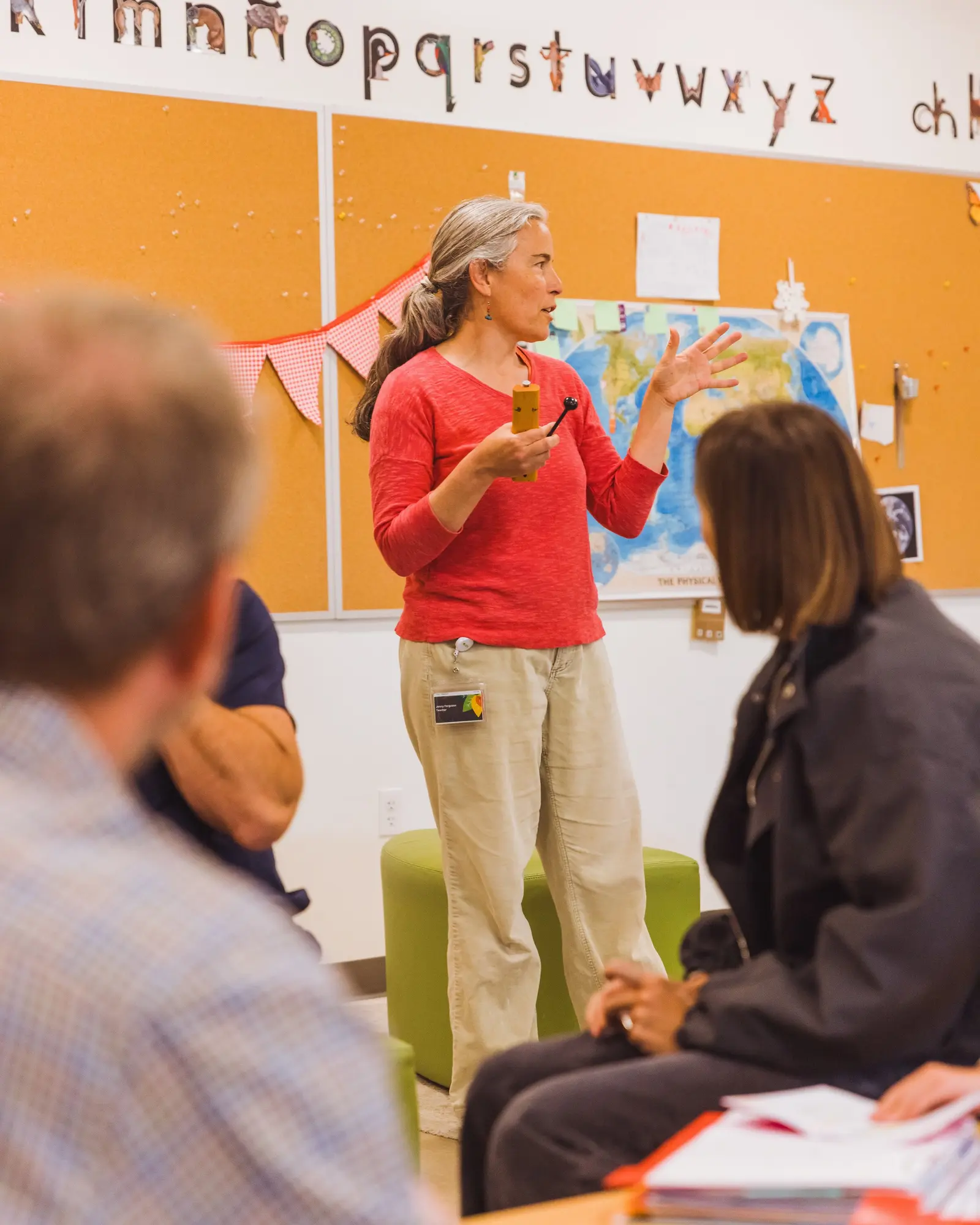 An instructor stands and speaks to a group of people in a classroom setting.