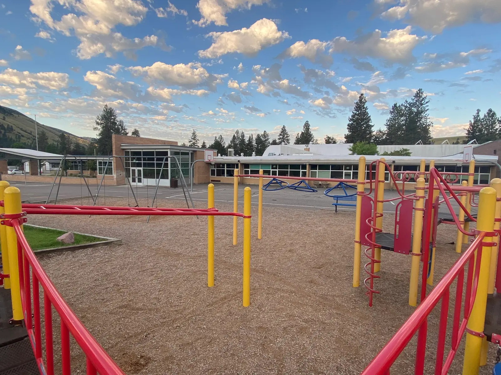 A view of a playground with climbing structures in the foreground and a school building in the background.