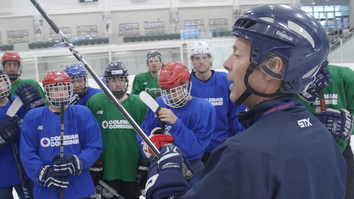An ice hockey coach gives instructions to a group of players at an indoor rink.