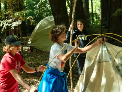 Three campers working together to set up a tent in the woods.