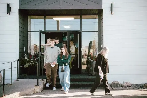 A group of young adults exits a building through glass doors.