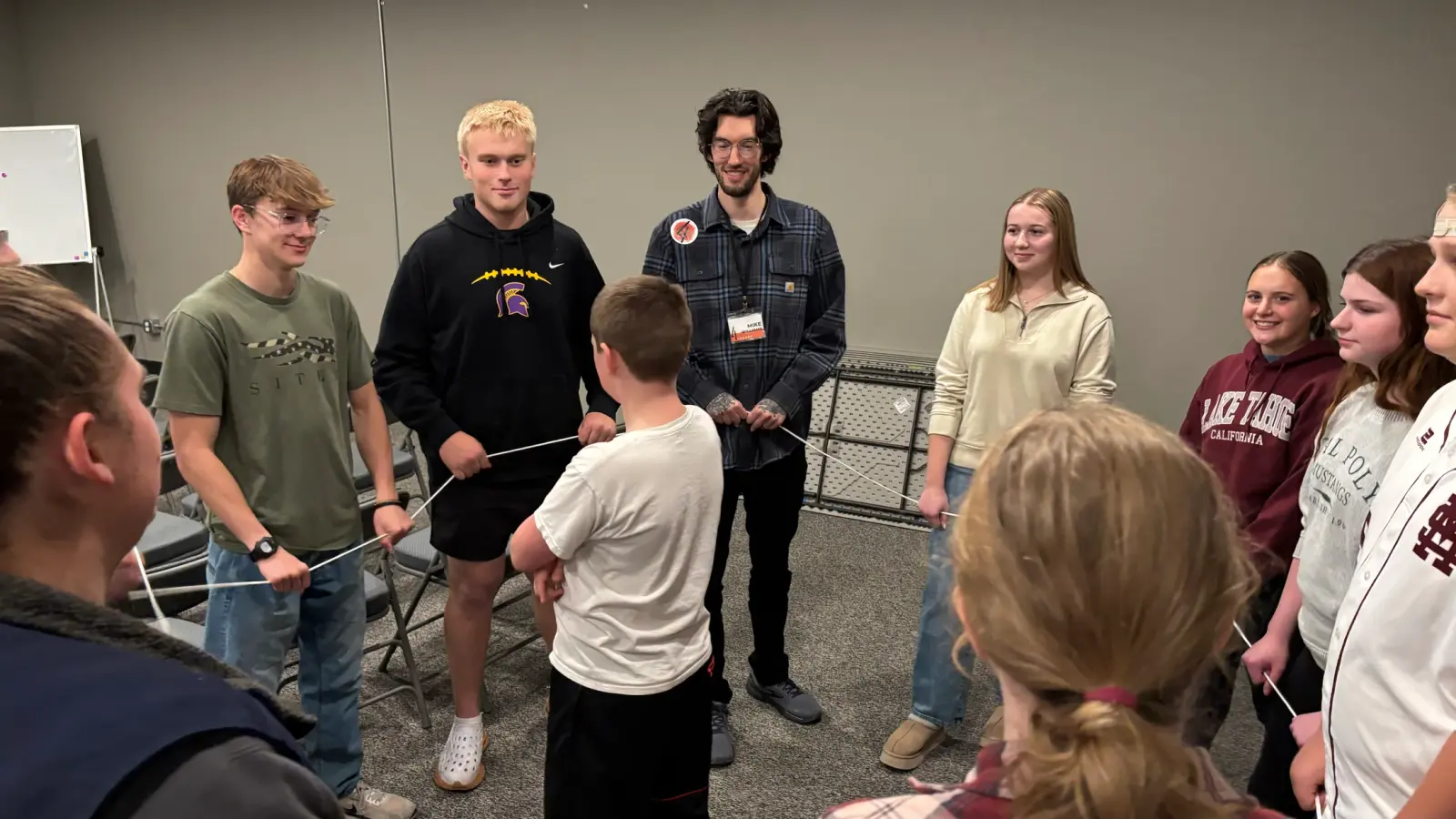 A group of young people and an instructor participate in a team-building exercise holding a string.