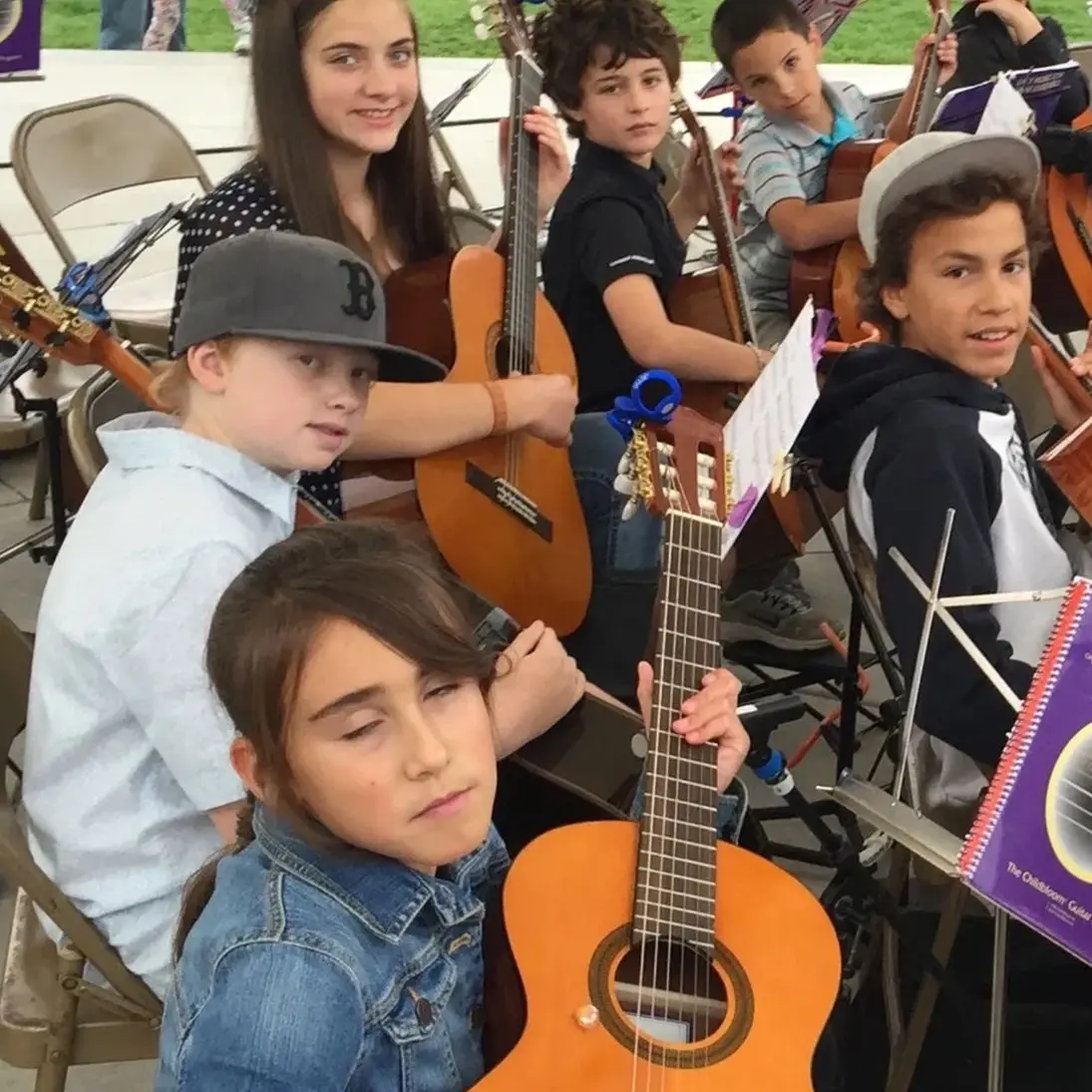 Group of kids playing guitars at an outdoor event.