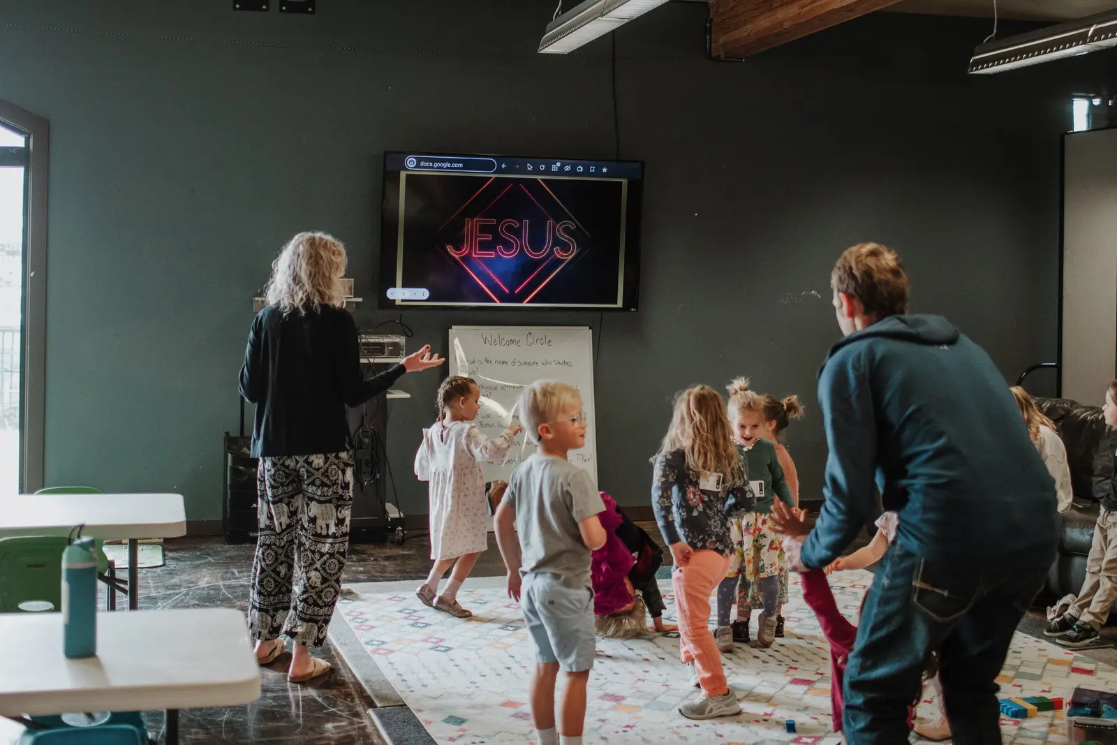 Adults lead a group of children in an indoor activity space.