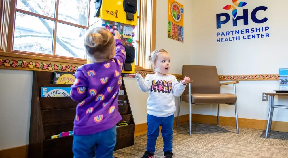 Two children are in a waiting area with books and a toy dispenser.