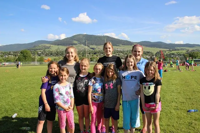 A group of young girls poses for a photo on a grassy athletic field.