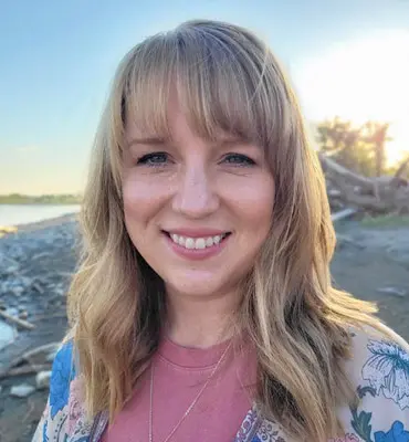 A woman smiles while outdoors near a body of water.