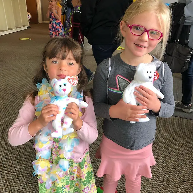 Two young girls are holding stuffed toy bears.