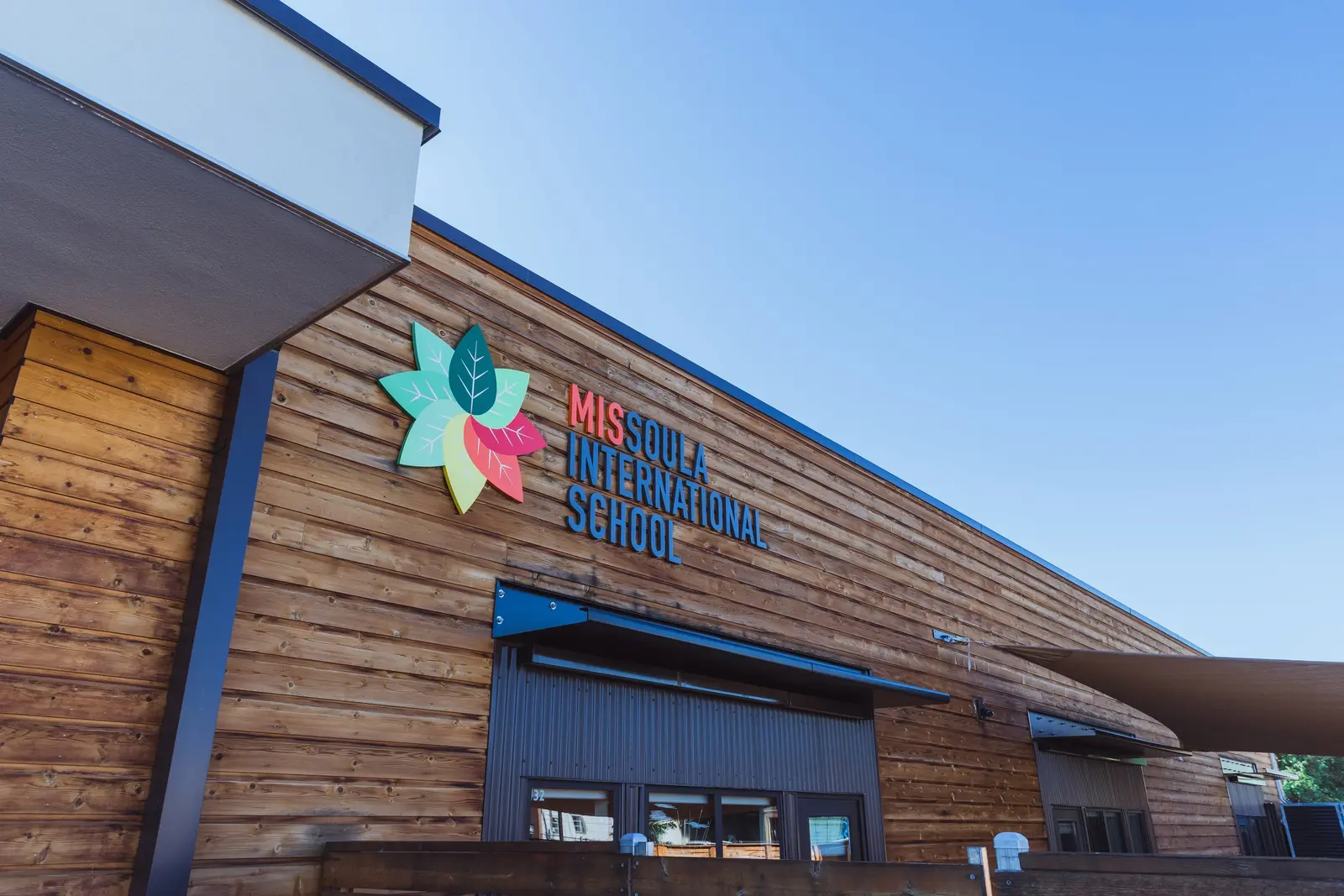 The exterior of a school building featuring wooden siding and a colorful logo with text.