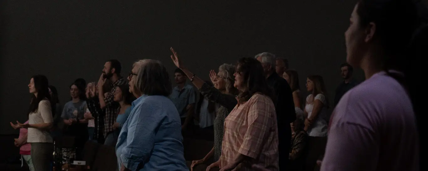 A group of people are standing in a dimly lit room with some of them raising their hands.