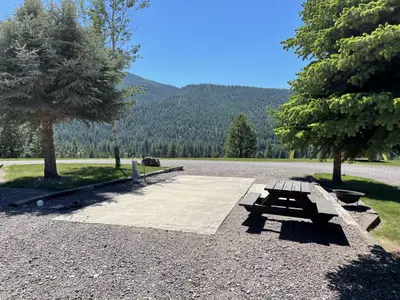 Photo from thenuggetrvresort.com A campsite with a concrete pad, a wooden picnic table, and a view of a forested mountain slope.