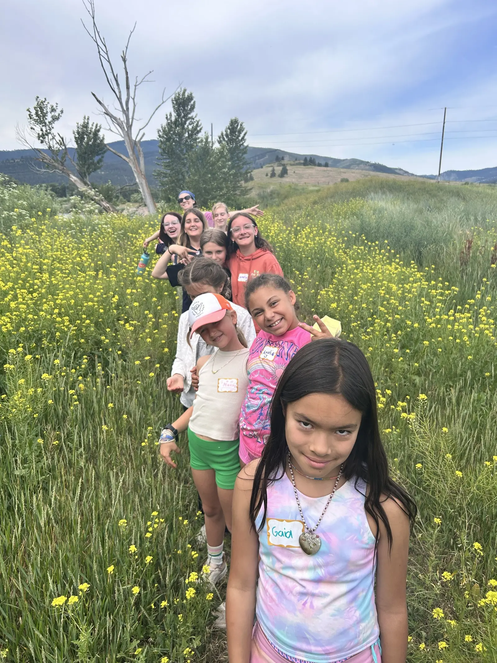 A group of children and teens are standing in a line in a meadow of yellow flowers.