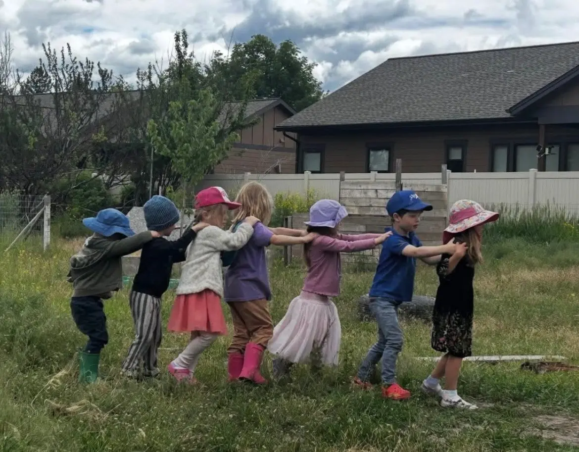 A line of children walking together while holding onto the shoulders of the child in front of them.