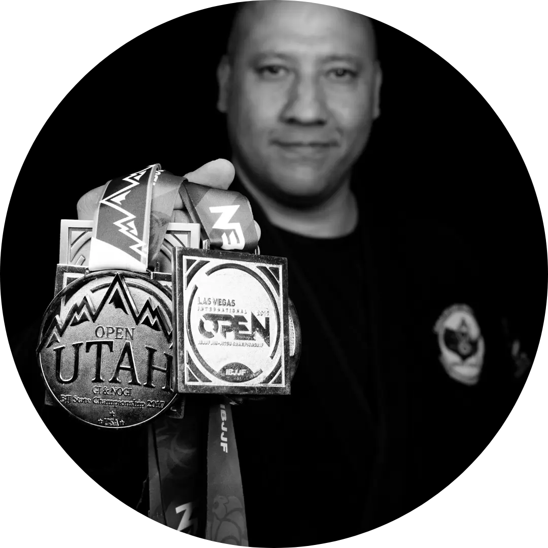 A man in a martial arts uniform holds up several medals from competitions.