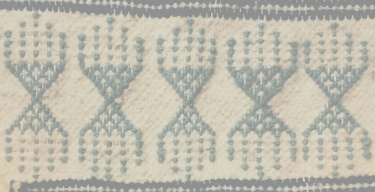 A close-up view shows a repeating woven geometric pattern in blue on a cream-colored textile.