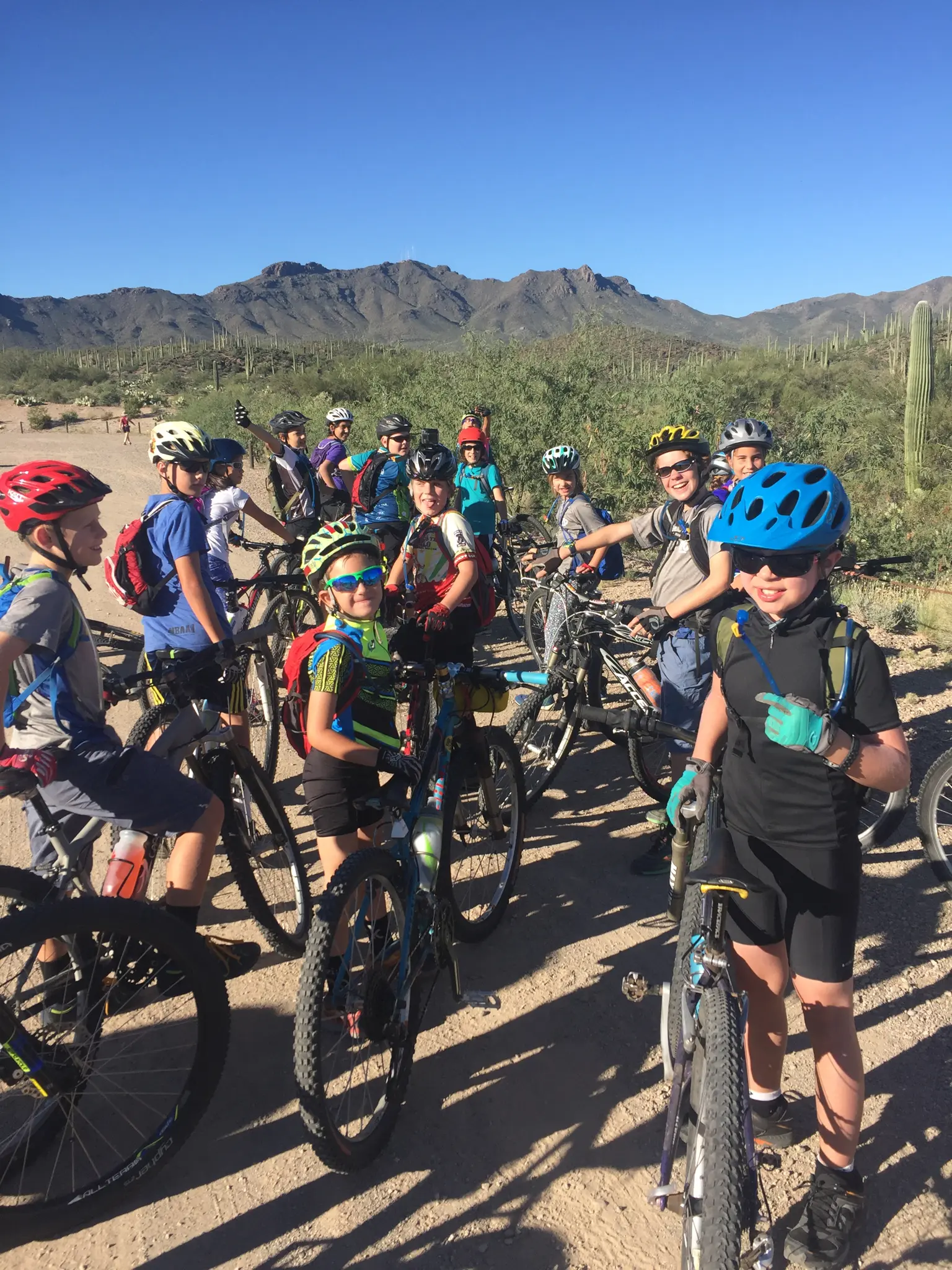 A group of children in cycling gear stands with their mountain bikes in a desert landscape.