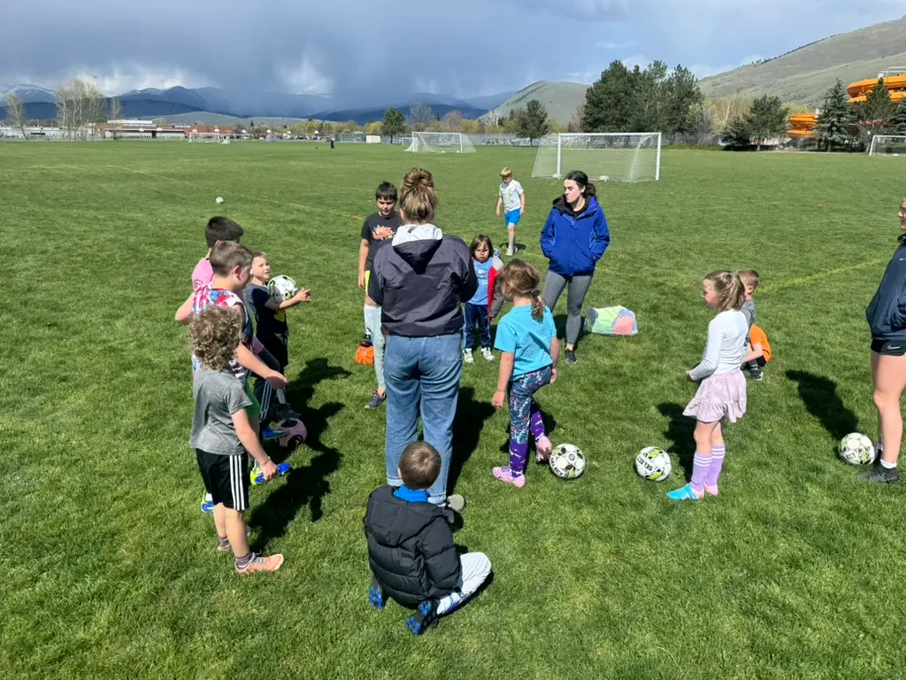 A group of children and instructors practice soccer on a large grassy field.