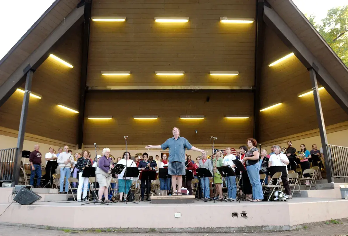 A conductor leads a concert band performing on an outdoor stage.