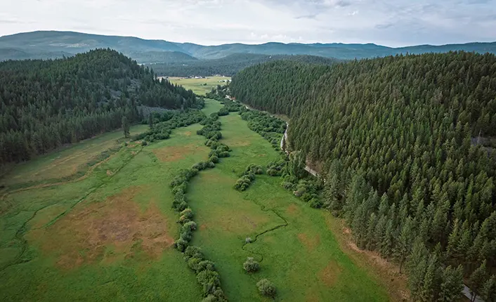 An aerial view shows a green valley winding through forested hills.
