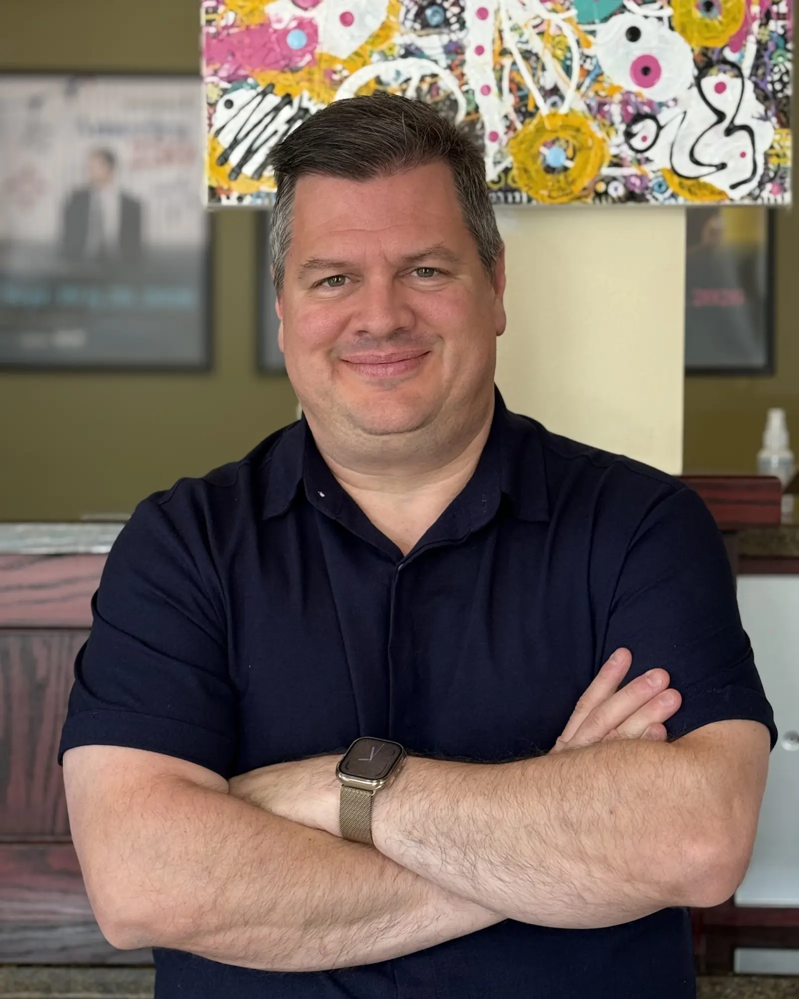 A man wearing a dark shirt stands with his arms crossed.