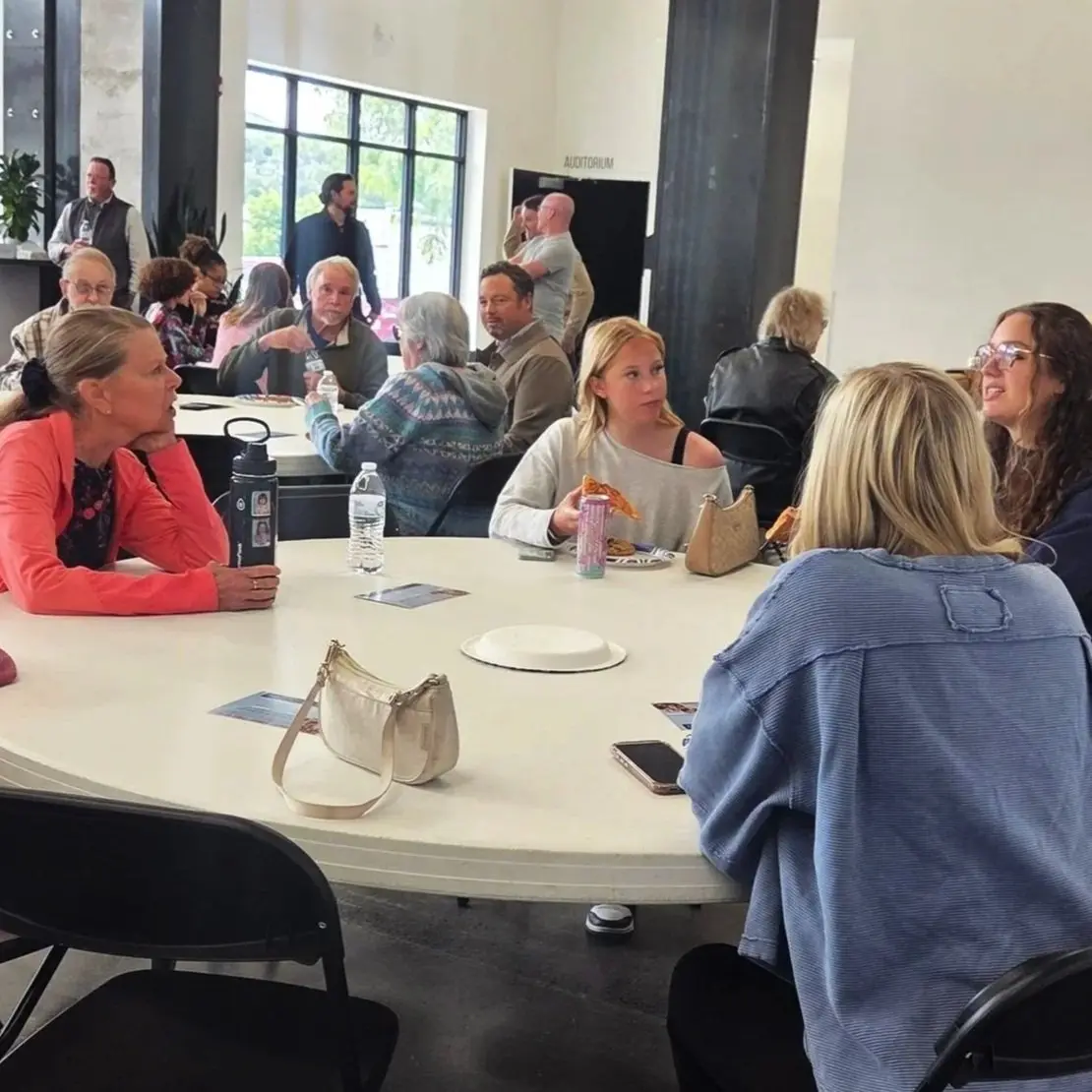A group of people sitting at circular tables in a bright, modern indoor space eating and talking.