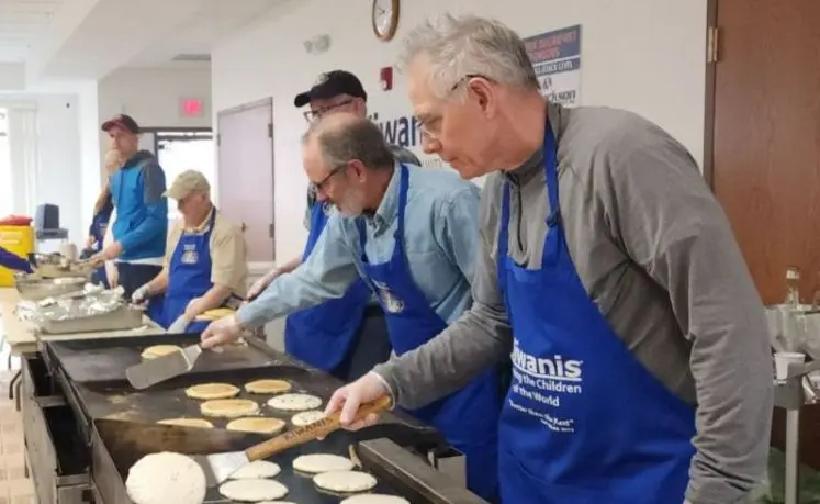 A group of men wearing blue aprons are cooking pancakes on a large griddle.