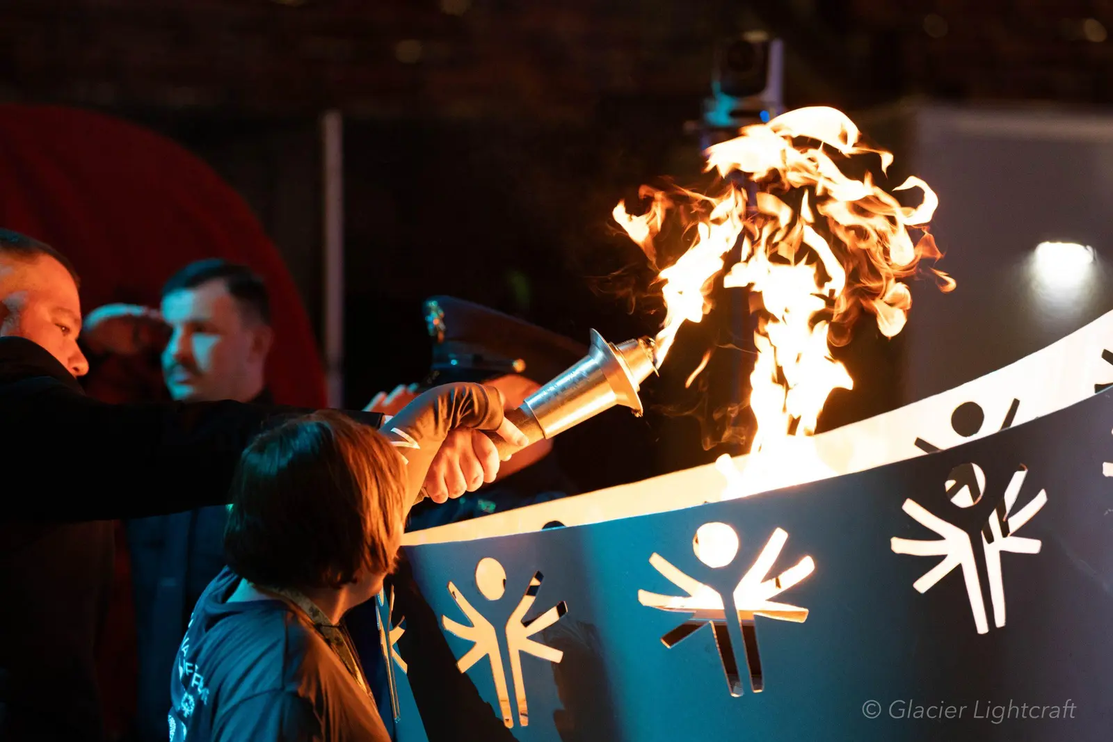 A person uses a torch to light a ceremonial cauldron as others look on.