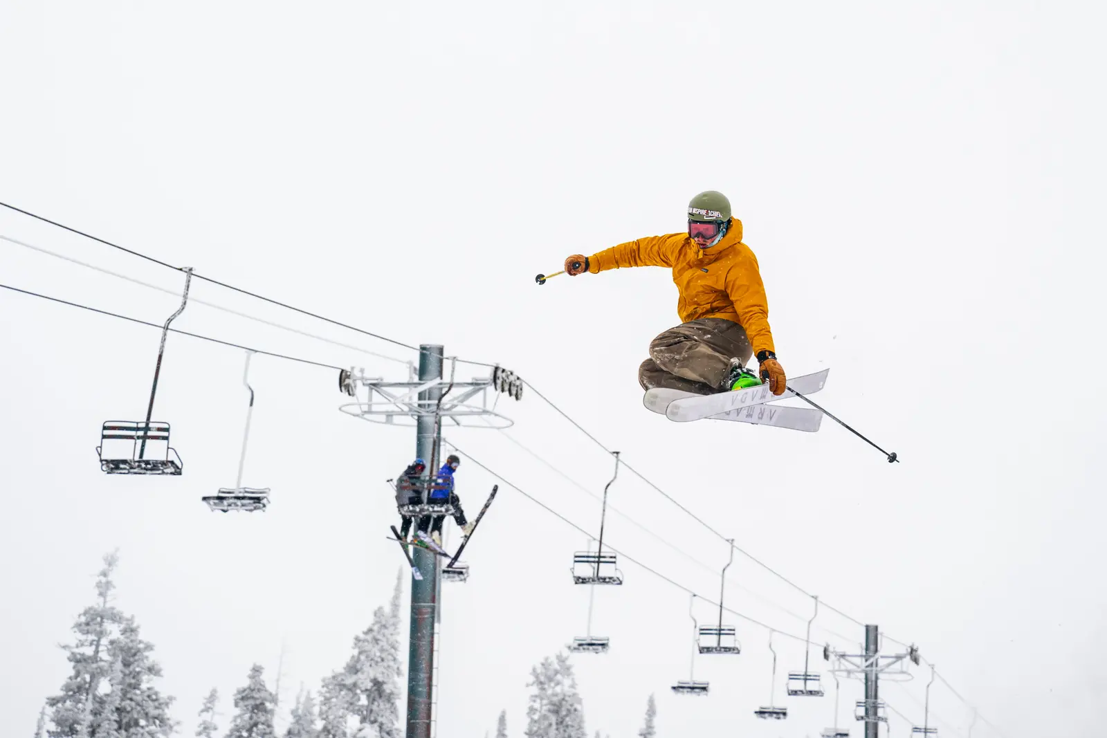 A skier performs a jump in the air in front of a chairlift.