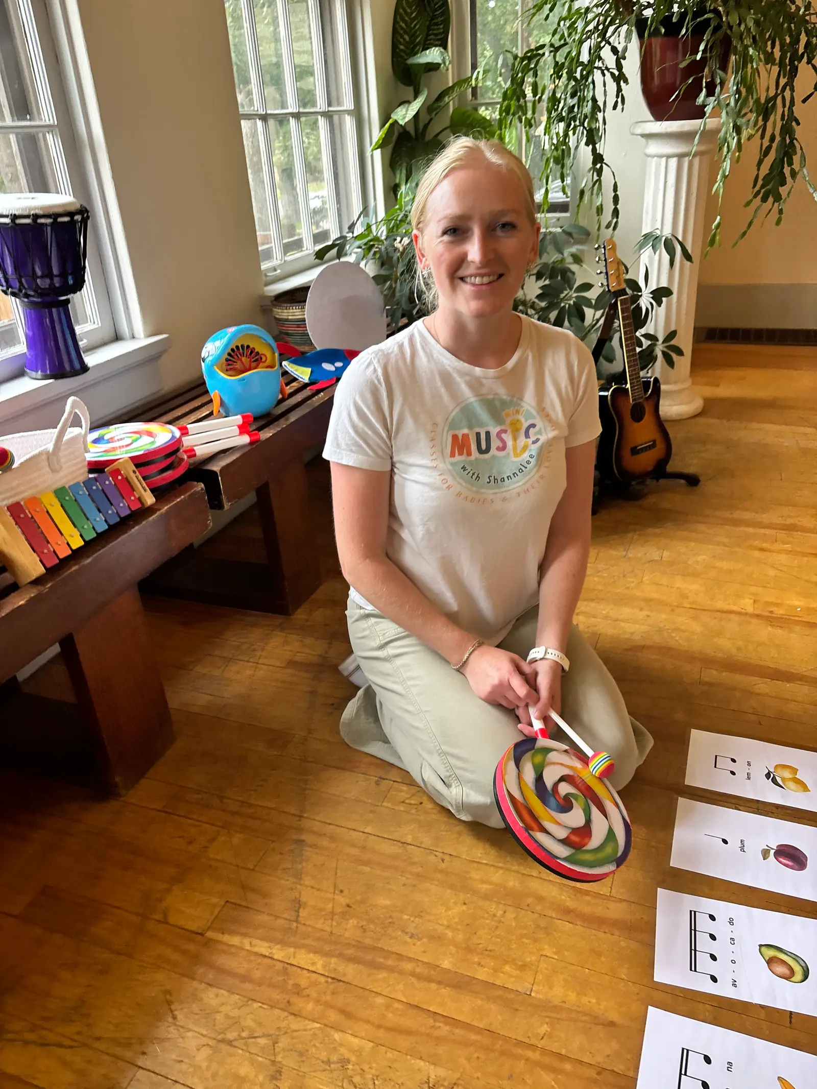 An instructor kneels on a wooden floor with musical instruments and teaching cards.
