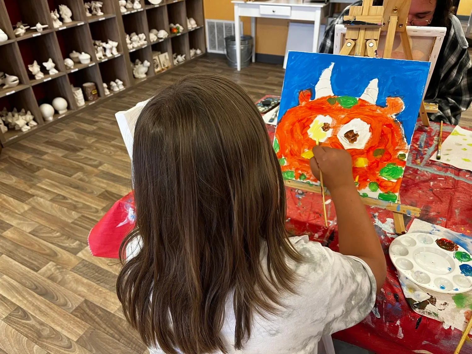 A child paints a picture of an orange monster on a canvas in a studio.