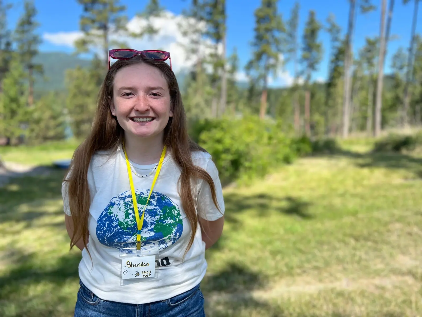A woman smiles while standing outdoors wearing a white t-shirt and a name tag.