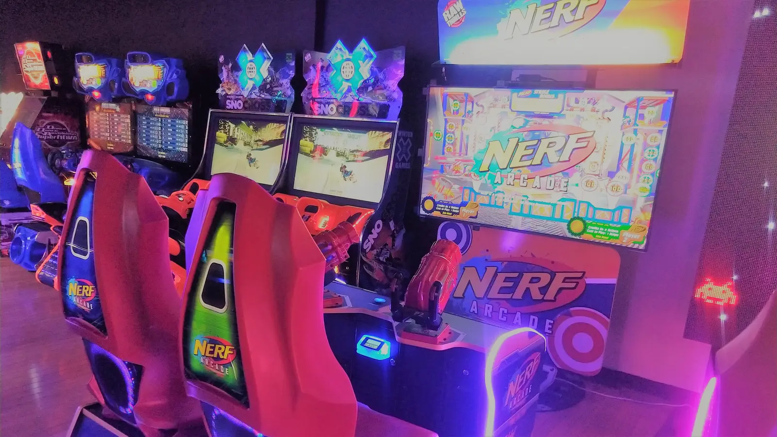 A collection of arcade games, including several Nerf Arcade units, are set up in a dimly lit room.
