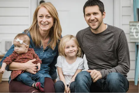 A smiling family sits on their steps with their daughter and foster daughter.