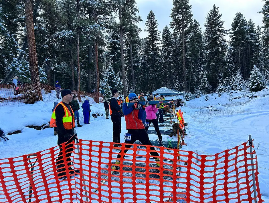People are practicing shooting with rifles while wearing skis on a snow-covered course in a forest.
