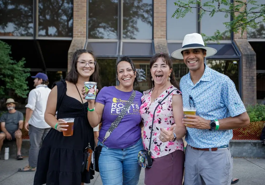 Four adults smiling and holding drinks while posing for a photograph outdoors.