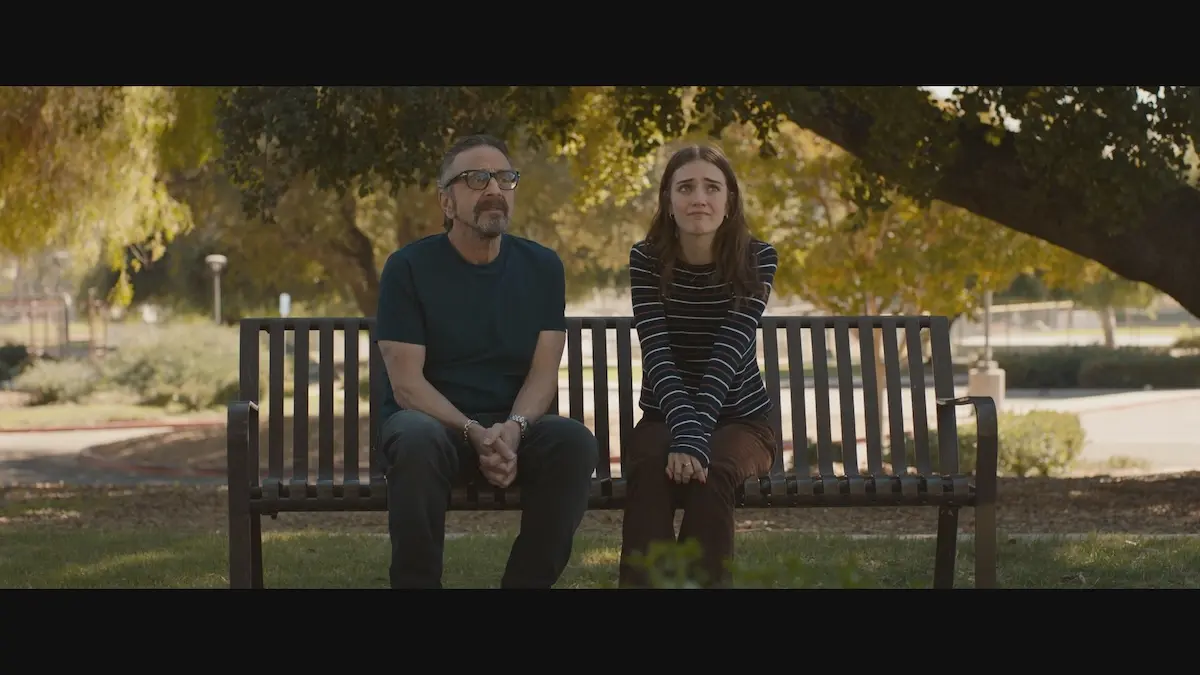 A man and a young woman sit side-by-side on a park bench.