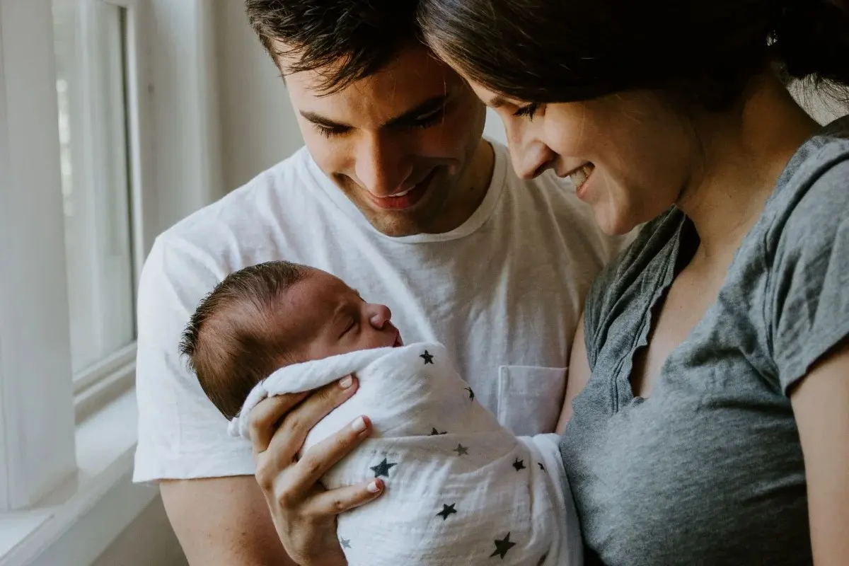 A mother and father lovingly look down at their newborn baby wrapped in a star-patterned swaddle.
